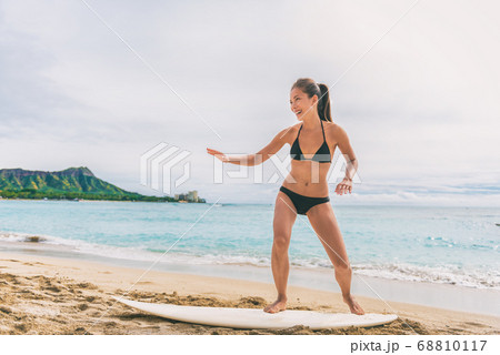 Asian tourist woman on Hawaii beach learning to surf at surfing school in Waikiki, Honolulu, Oahu. Girl having fun practicing on surfboard on shore Asian tourist woman on Hawaii beach learning to surf at surfing school in Waikiki, Honolulu, Oahu. Girl having fun practicing on surfboard on shore 68810117