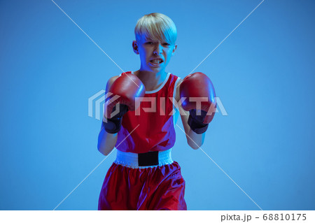 Teenager in sportswear boxing isolated on blue studio background in neon light Teenager in sportswear boxing isolated on blue studio background in neon light 68810175