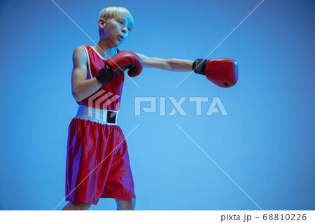 Teenager in sportswear boxing isolated on blue studio background in neon light Teenager in sportswear boxing isolated on blue studio background in neon light 68810226