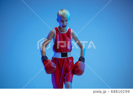 Teenager in sportswear boxing isolated on blue studio background in neon light 68810299
