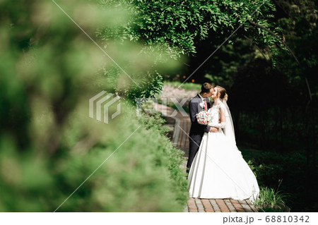 Beautiful bride and groom embracing and kissing on their wedding day outdoors 68810342