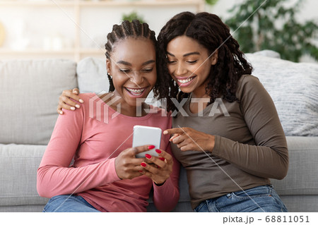 Cheerful black girls having fun at home, using smartphone 68811051