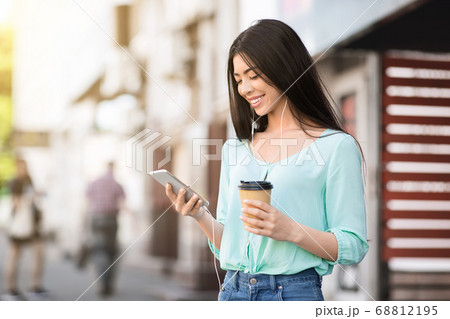 Happy asian girl listening to music while walking outdoors with takeaway coffee Happy asian girl listening to music while walking outdoors with takeaway coffee 68812195