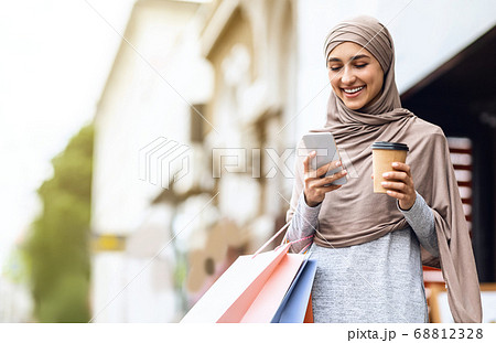 Cheerful arab girl in hijab with shopping bags using phone 68812328