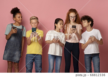 Modern technologies in schooling. Multiethnic kids using cellphones together over pink background Modern technologies in schooling. Multiethnic kids using cellphones together over pink background 68812336
