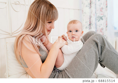 mom sitting on bed with baby and playing with son 68815514