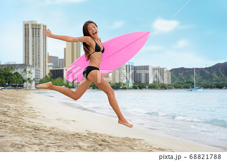 Surfing summer fun woman jumping of joy on beach with surfboard. Surf vacation lifestyle. Asian girl in bikini, sport and fitness active concept. 68821788