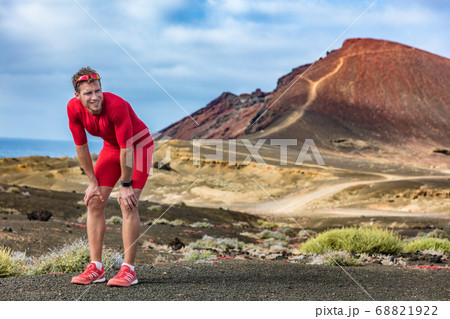 Tired runner on trail run feeling exhausted and dehydrated from the heat. Athlete man with smartwatch taking a break catching his breath looking at challenge ahead. Tired runner on trail run feeling exhausted and dehydrated from the heat. Athlete man with smartwatch taking a break catching his breath looking at challenge ahead. 68821922