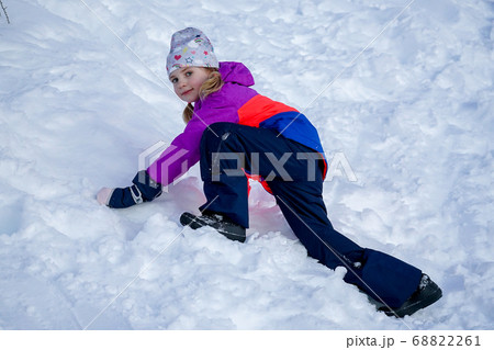 Outdoor winter portrait of little cute girl wearing ski clothes. Girl climbing a snow slide. 68822261