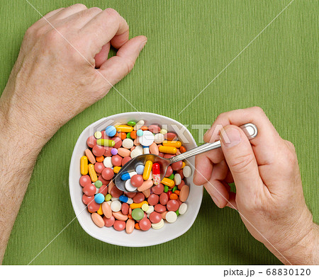 Person eats a lot of pills, tablets, capsules from a bowl with a spoon at the dinner table. Top view. 68830120