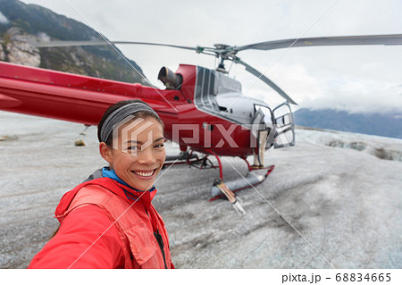 Happy tourist taking selfie picture on helicopter tour excursion. Asian woman cruise passenger on shore activity glacier walk hike in Alaska, USA. 68834665