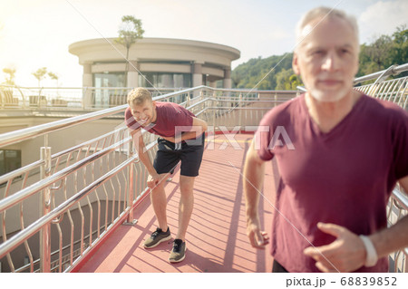 Grey-haired male running across bridge, young male holding hand on his chest behind him Grey-haired male running across bridge, young male holding hand on his chest behind him 68839852