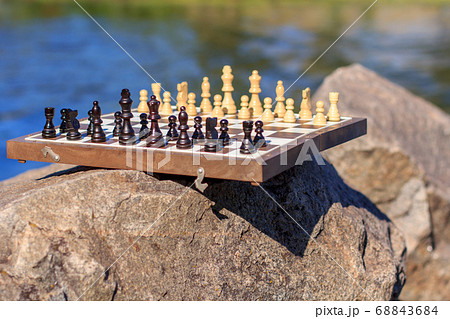 Chess board with chess pieces on rock with river Chess board with chess pieces on rock with river 68843684
