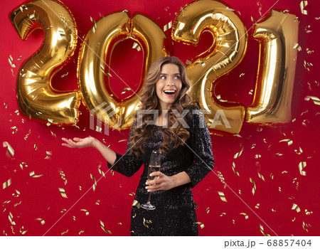 Sexy millennial woman wearing elegant dress and celebrating 2021 with champagne and confetti, red background Sexy millennial woman wearing elegant dress and celebrating 2021 with champagne and confetti, red background 68857404