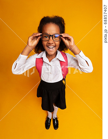 African Schoolgirl Looking At Camera Through Eyeglasses On Yellow Background 68857407
