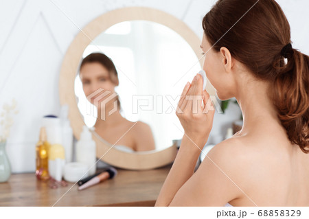 Young woman applying face toner on her face 68858329
