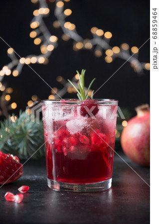 Pomegranate Christmas cocktail with sparkling wine garnish rosemary sprig on holiday dark background with garland. 68859464