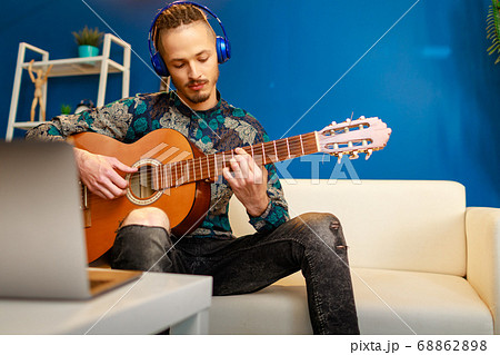 Young stylish caucasian man taking guitar class online at home using his laptop Young stylish caucasian man taking guitar class online at home using his laptop 68862898