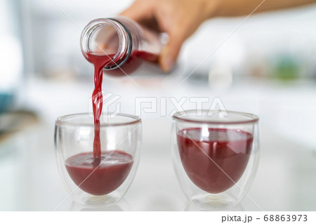 Juice bottle beet drink smoothie woman pouring drinks in cups at home kitchen. Closeup of two glasses with red vegetable juicing cold pressed beverage Juice bottle beet drink smoothie woman pouring drinks in cups at home kitchen. Closeup of two glasses with red vegetable juicing cold pressed beverage 68863973