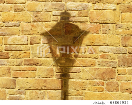 Closeup photo of an illuminated orange-yellow brick wall with a falling shadow from a lantern on it 68865932