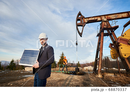 Oil worker in helmet holding solar panel. 68870337