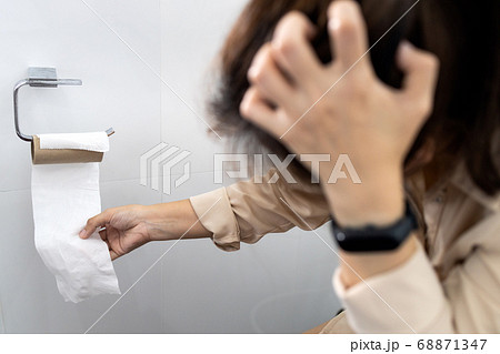 Stressed woman sitting on toilet bowl with tissue roll that was about to run out,effects from the Coronavirus,problem of tissue paper is out of stock during outbreak of Covid-19,out of toilet paper 68871347