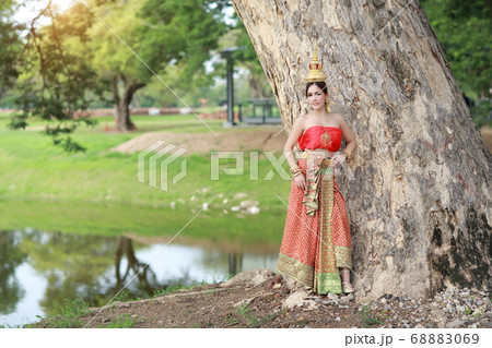 young asian fashion girl wearing Thai traditional costume with beauty face standing beside big trees 68883069