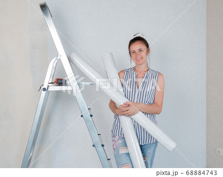 Portrait of a happy woman with rolls of Wallpaper in her hands is leaning on a stepladder. Renovation of the room. Portrait of a happy woman with rolls of Wallpaper in her hands is leaning on a stepladder. Renovation of the room. 68884743