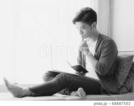 Young Asian man writing in a book when using 68887502