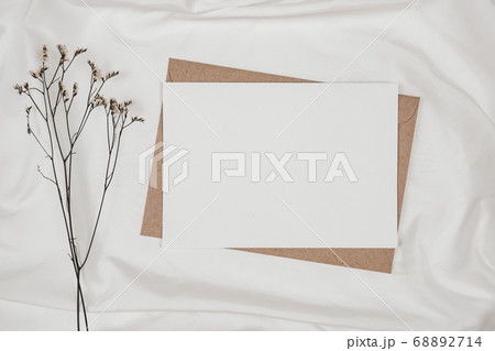 Blank white paper on brown paper envelope with Limonium dry flower on white cloth. Mock-up of horizontal blank greeting card. Top view of Craft envelope on white background. Flat lay minimalism Blank white paper on brown paper envelope with Limonium dry flower on white cloth. Mock-up of horizontal blank greeting card. Top view of Craft envelope on white background. Flat lay minimalism 68892714