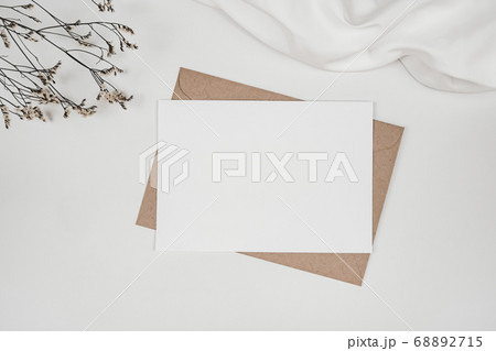 Blank white paper on brown paper envelope with Limonium dry flower and white cloth. Mock-up of horizontal blank greeting card. Top view of Craft envelope on white background. Flat lay minimalism Blank white paper on brown paper envelope with Limonium dry flower and white cloth. Mock-up of horizontal blank greeting card. Top view of Craft envelope on white background. Flat lay minimalism 68892715