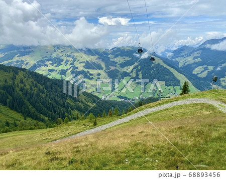 View towards Saalbach village and mountains in Saalbach-Hinterglemm skiing region in Austria on a beautiful summer day with cableway and lush meadows used by cows for grazing View towards Saalbach village and mountains in Saalbach-Hinterglemm skiing region in Austria on a beautiful summer day with cableway and lush meadows used by cows for grazing 68893456