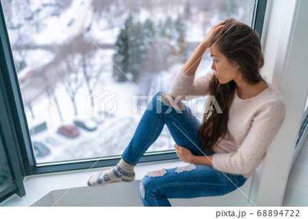Winter depressed sad girl lonely by home window looking at cold weather upset unhappy. Bad feelings stress, anxiety, grief, emotions. Asian woman portrait 68894722