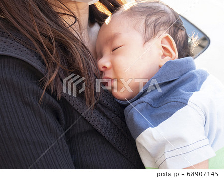 母親に抱っこされて眠る生後1ヶ月の新生児の赤ちゃんの写真素材 