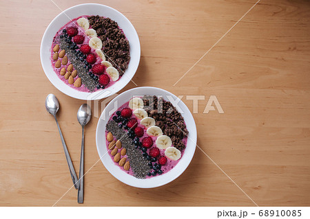 Smoothie bowl with fresh raspberry, blueberry, chia seeds, almonds, banana, and chocolate flakes. Morning breakfast on wooden table. Top view of two plates. vegan food Smoothie bowl with fresh raspberry, blueberry, chia seeds, almonds, banana, and chocolate flakes. Morning breakfast on wooden table. Top view of two plates. vegan food 68910085