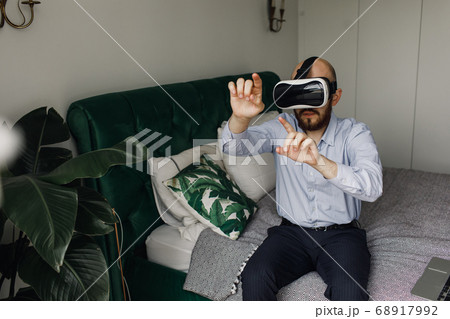 young man with a beard in virtual reality glasses sits on the edge of the bed 68917992