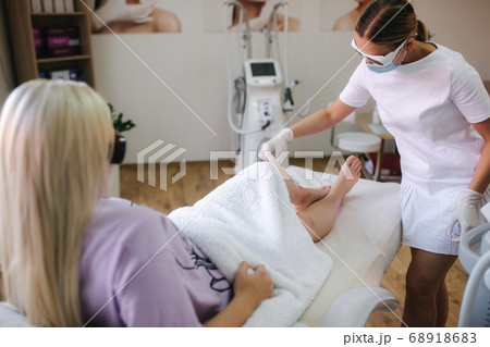 Young woman beautician in mask applies contact gel on the leg of a woman for laser hair removal in medical clinic 68918683