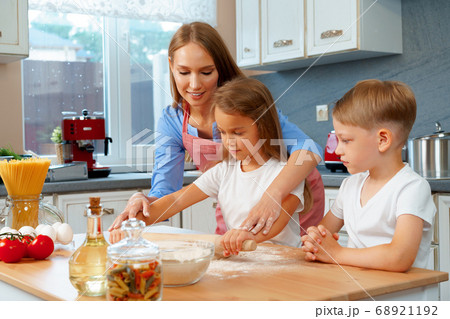 Mother and her little kids, boy and girl, helping her to prepare dough Mother and her little kids, boy and girl, helping her to prepare dough 68921192