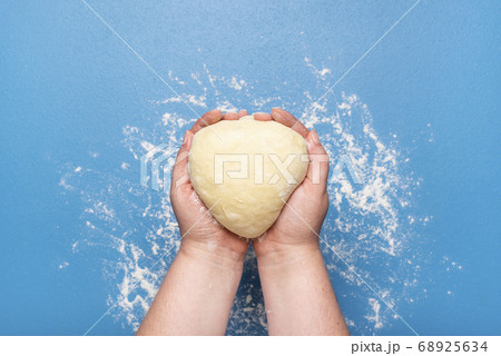 Raw dough held in hands over blue color. Uncooked Raw dough held in hands over blue color. Uncooked 68925634