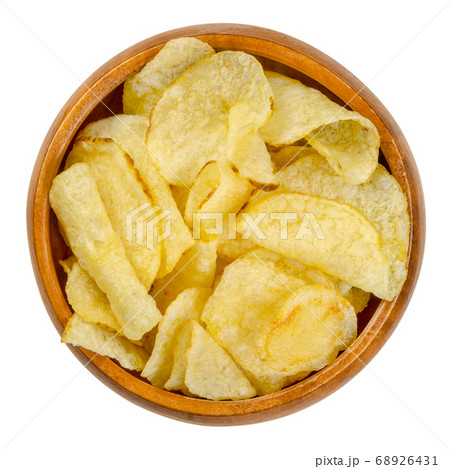 Salted potato chips with peel, also crisps, in wooden bowl. Thin slices of potato, deep fried in oil until crunchy. Served as snack, side dish or appetizer. Close-up from above over white, food photo. Salted potato chips with peel, also crisps, in wooden bowl. Thin slices of potato, deep fried in oil until crunchy. Served as snack, side dish or appetizer. Close-up from above over white, food photo. 68926431
