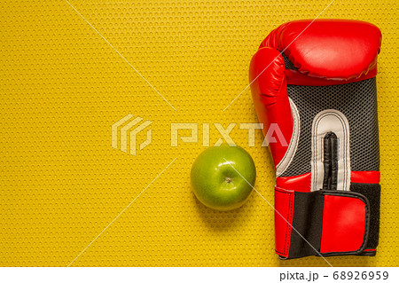 Top view of a green apple and red boxing glove on the yellow mat. Sport at home, fitness practice Top view of a green apple and red boxing glove on the yellow mat. Sport at home, fitness practice 68926959