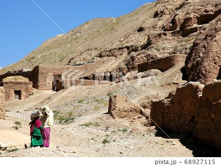 Bamyan (Bamiyan) in Central Afghanistan. A woman and girl carry goods on their heads as they walk home. These local houses are close to the Bamyan (Bamiyan) Buddhas. Local life Afghanistan. 68927115