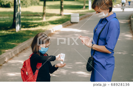 Mother in protective mask applies sanitizer on daughter's hands. 68928136