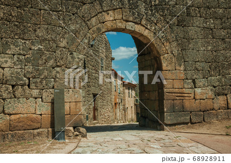 Old house seen through arch gate from a stone wall 68928911