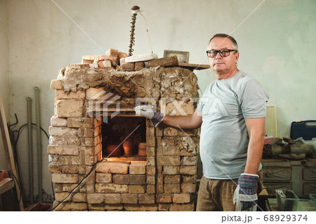 Potter stands on background of brick oven. Potter stands on background of brick oven. 68929374
