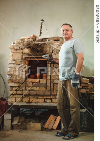 Potter stands on background of brick oven. Potter stands on background of brick oven. 68930080