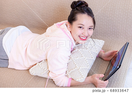 ソファーに寝転んでタブレットを見る女性 68933647