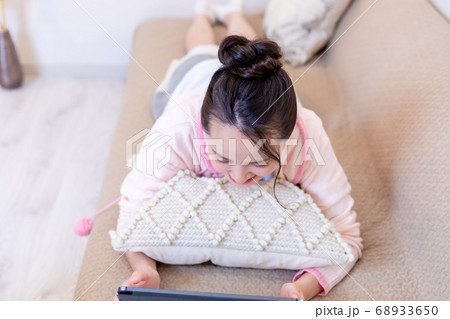 ソファーに寝転んでタブレットを見る女性 68933650