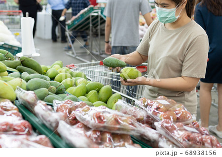 Asian woman wear a face mask,chooses necessary food,mango,fruit while shopping at supermarket,people panic buying, hoarding during the Covid-19,Coronavirus spread,girl preparing for pandemic,stay home Asian woman wear a face mask,chooses necessary food,mango,fruit while shopping at supermarket,people panic buying, hoarding during the Covid-19,Coronavirus spread,girl preparing for pandemic,stay home 68938156