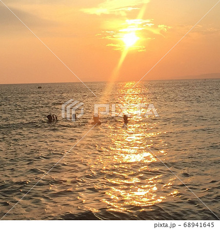 夕焼け空と夕日が当たる海の中で泳ぐ人々の写真素材